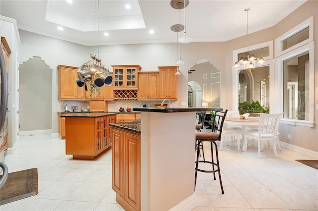 kitchen featuring pendant lighting, dark stone countertops, a kitchen bar, a center island, and a raised ceiling