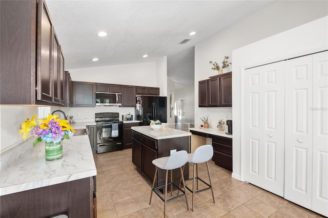 kitchen with a breakfast bar area, vaulted ceiling, light tile patterned floors, a kitchen island, and black appliances