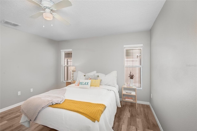 bedroom with ceiling fan, a textured ceiling, multiple windows, and light wood-type flooring