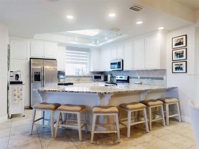 kitchen featuring white cabinetry, appliances with stainless steel finishes, a kitchen breakfast bar, and light stone counters