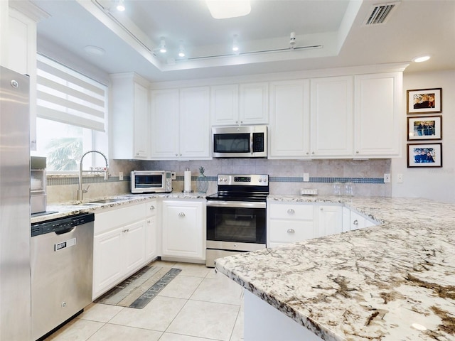 kitchen with sink, light tile patterned floors, appliances with stainless steel finishes, a tray ceiling, and white cabinets