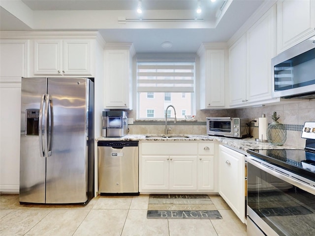 kitchen with light stone counters, stainless steel appliances, sink, and white cabinets