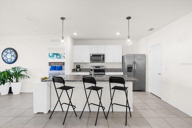 kitchen featuring appliances with stainless steel finishes, a kitchen breakfast bar, a center island with sink, decorative light fixtures, and dark stone counters