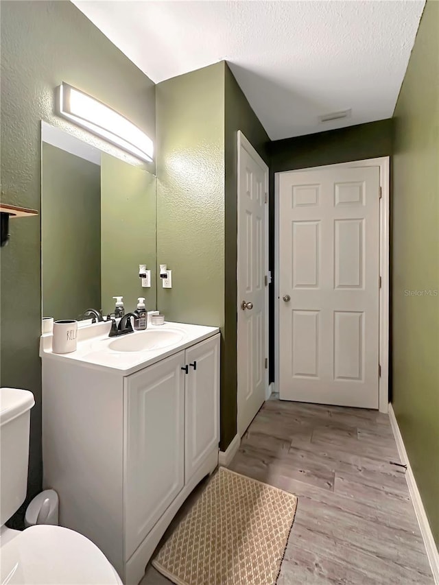 bathroom featuring wood-type flooring, toilet, vanity, and a textured ceiling