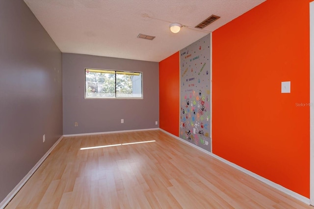 spare room featuring a textured ceiling and light hardwood / wood-style floors