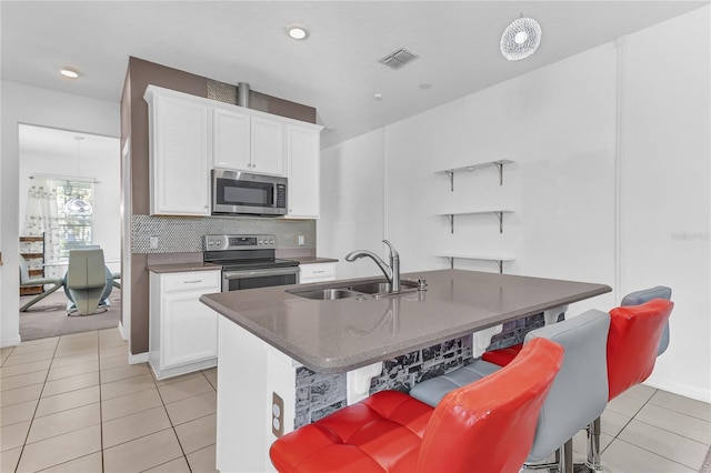 kitchen with a kitchen bar, sink, a center island with sink, stainless steel appliances, and white cabinets