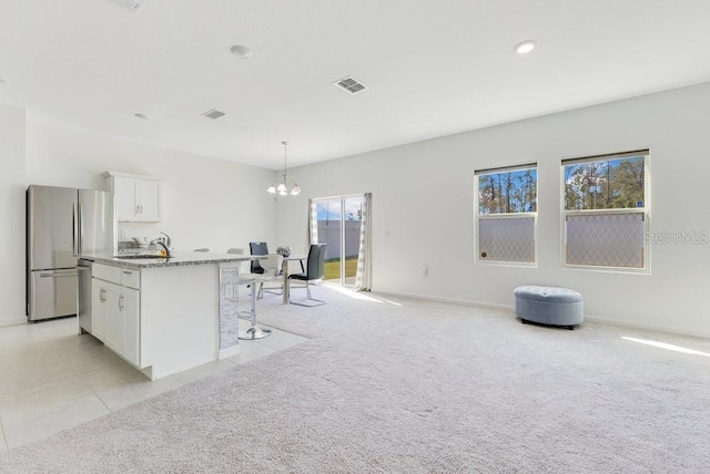 kitchen featuring appliances with stainless steel finishes, light stone counters, white cabinets, a center island with sink, and decorative light fixtures