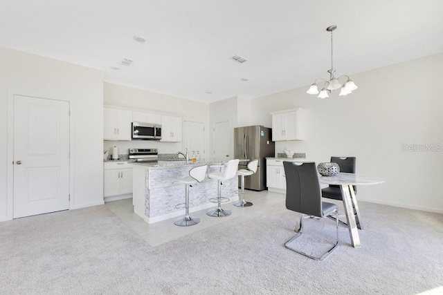 kitchen with appliances with stainless steel finishes, pendant lighting, white cabinets, a kitchen bar, and a kitchen island with sink