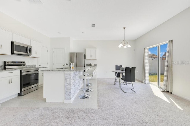 kitchen featuring pendant lighting, a center island with sink, white cabinets, and appliances with stainless steel finishes