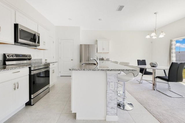 kitchen featuring appliances with stainless steel finishes, white cabinetry, hanging light fixtures, light stone counters, and an island with sink