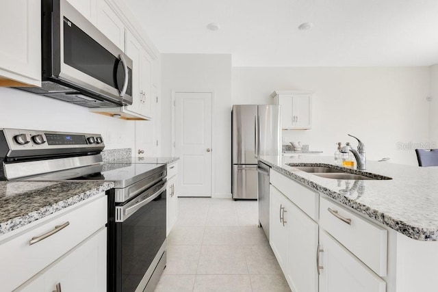 kitchen with sink, white cabinets, light tile patterned floors, stainless steel appliances, and a center island with sink