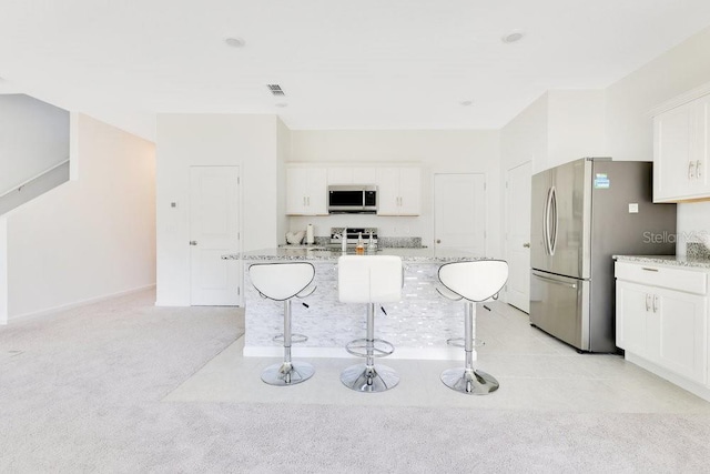 kitchen with white cabinetry, appliances with stainless steel finishes, light stone countertops, and a kitchen island with sink