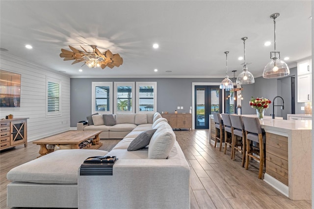 living room featuring crown molding, sink, wooden walls, and light hardwood / wood-style floors