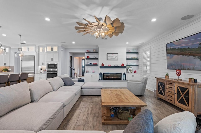 living room with a large fireplace, ornamental molding, wooden walls, ceiling fan, and hardwood / wood-style floors