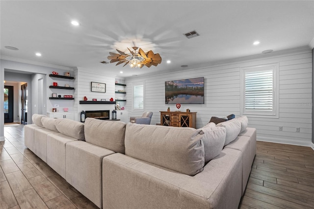 living room featuring crown molding, hardwood / wood-style flooring, wooden walls, and a large fireplace