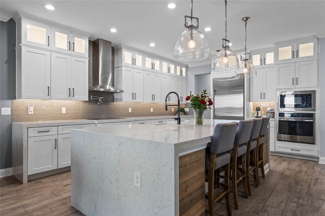 kitchen with built in appliances, white cabinets, and wall chimney exhaust hood