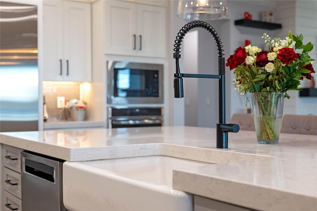 kitchen with white cabinetry, stainless steel appliances, light stone countertops, and sink