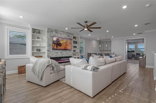 living room featuring crown molding, built in features, a fireplace, and light hardwood / wood-style floors