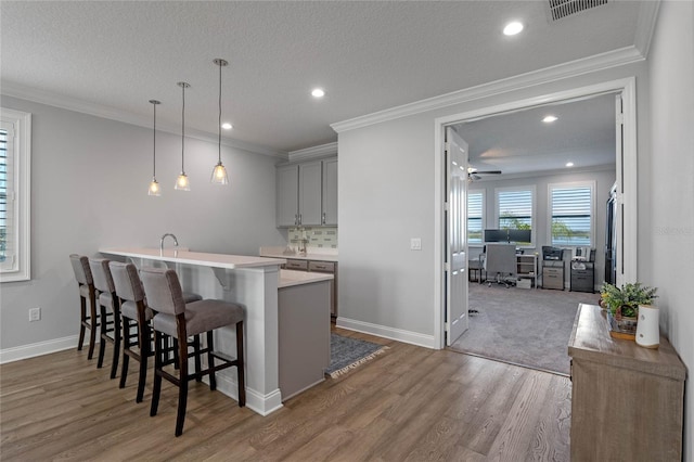 kitchen with gray cabinetry, wood-type flooring, decorative light fixtures, a kitchen breakfast bar, and decorative backsplash