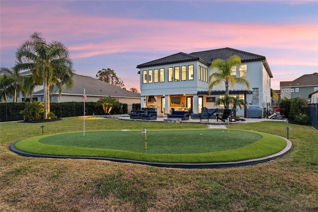 back house at dusk featuring an outdoor hangout area, a patio, and a lawn