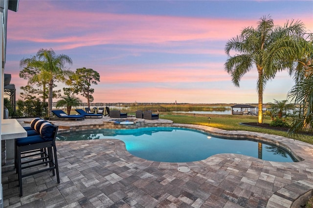 pool at dusk with a patio area, an in ground hot tub, and a water view