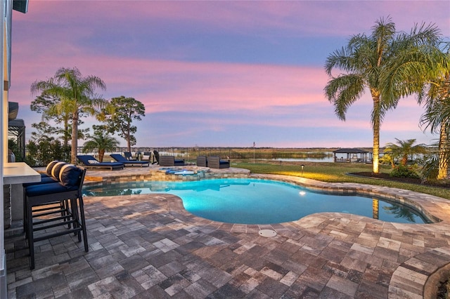 pool at dusk featuring an in ground hot tub and a patio