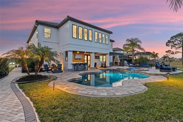 back house at dusk with a patio, a lawn, a bar, a swimming pool with hot tub, and a pergola