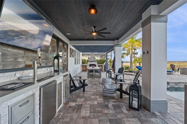 view of patio / terrace with ceiling fan, an outdoor kitchen, and an outdoor stone fireplace