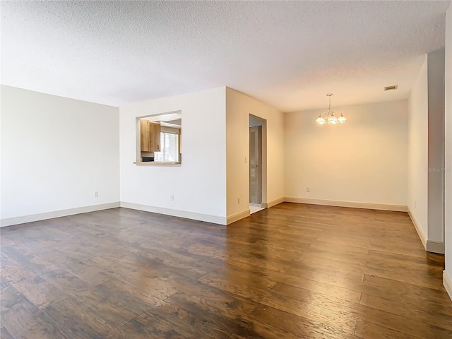 spare room featuring dark wood-type flooring, a textured ceiling, and a notable chandelier