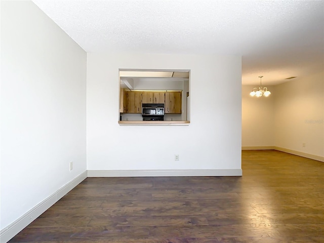 unfurnished room with a notable chandelier, dark hardwood / wood-style floors, and a textured ceiling