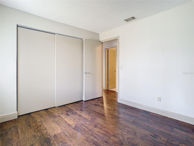 unfurnished bedroom featuring dark wood-type flooring, a closet, and a textured ceiling