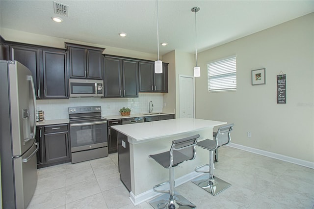 kitchen featuring pendant lighting, sink, appliances with stainless steel finishes, a kitchen island, and decorative backsplash