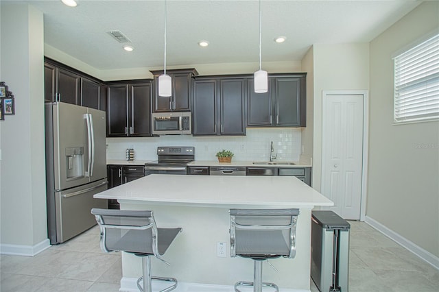 kitchen with a kitchen bar, sink, hanging light fixtures, appliances with stainless steel finishes, and a kitchen island