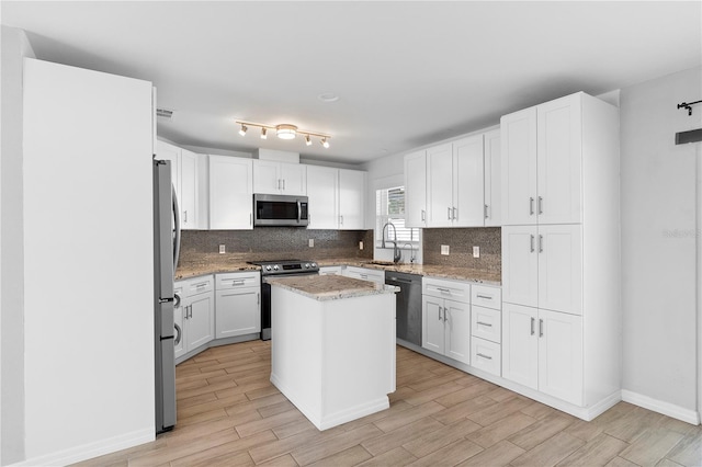 kitchen featuring white cabinetry, backsplash, stainless steel appliances, light stone counters, and a kitchen island