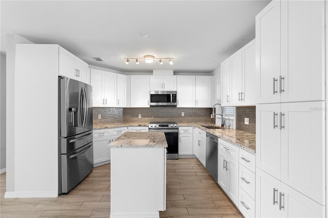 kitchen with sink, appliances with stainless steel finishes, a center island, light stone counters, and white cabinets