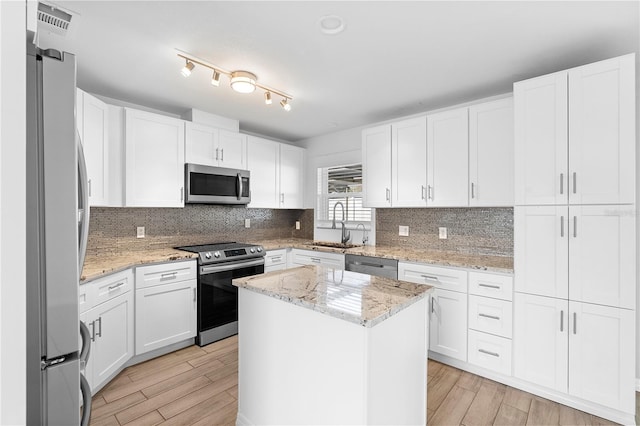 kitchen with light stone counters, stainless steel appliances, a center island, and white cabinets