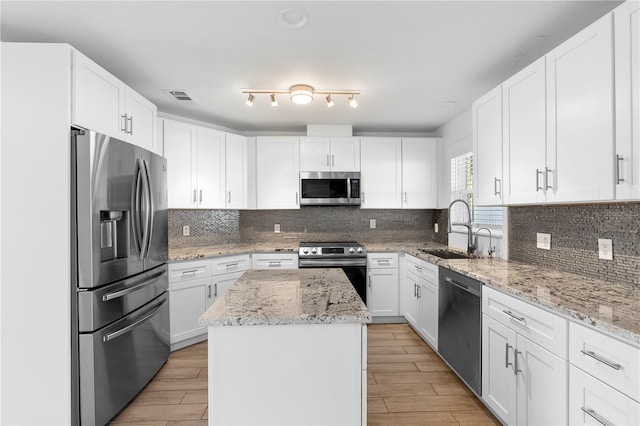 kitchen featuring sink, stainless steel appliances, a center island, light stone countertops, and white cabinets