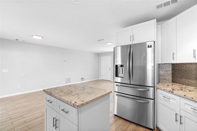 kitchen featuring white cabinetry, light stone counters, stainless steel fridge with ice dispenser, decorative backsplash, and light wood-type flooring