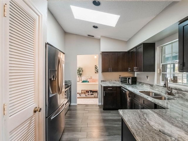 kitchen with sink, light stone counters, dark brown cabinets, dark hardwood / wood-style flooring, and stainless steel appliances