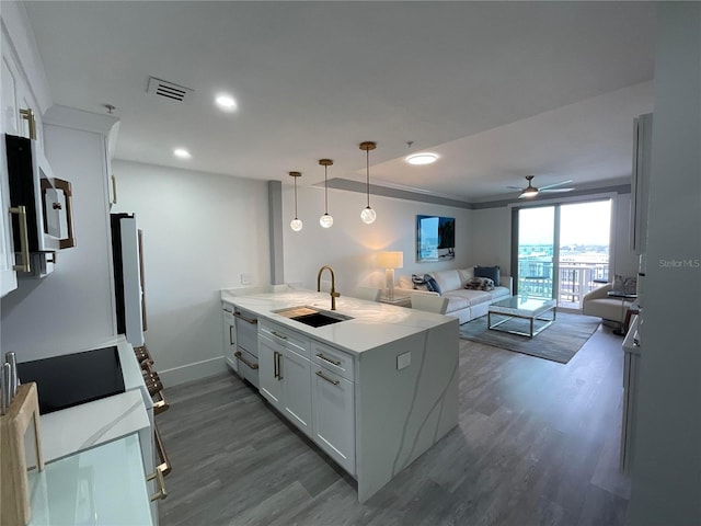 kitchen featuring dark wood-type flooring, sink, white cabinetry, decorative light fixtures, and kitchen peninsula