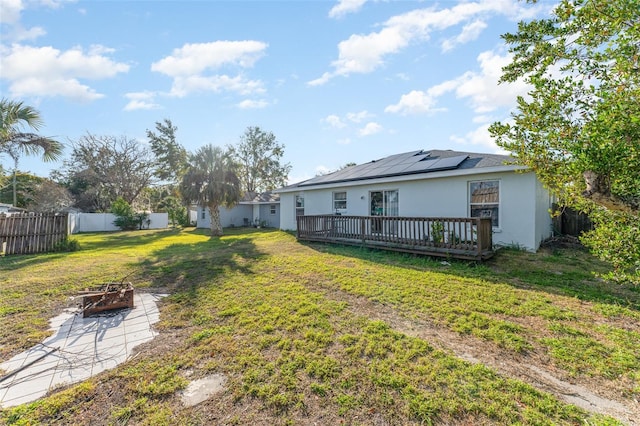 rear view of property with a wooden deck, a yard, a fire pit, and solar panels