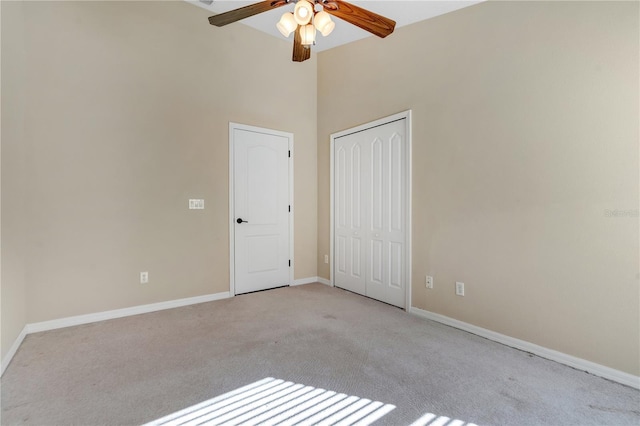 empty room with a high ceiling, light colored carpet, and ceiling fan