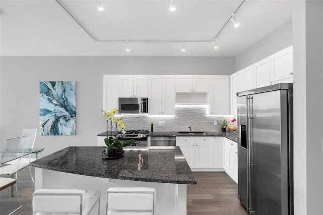 kitchen with white cabinetry, backsplash, stainless steel appliances, a kitchen island, and dark stone counters