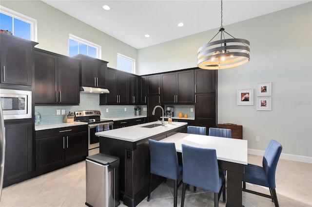 kitchen featuring sink, decorative backsplash, hanging light fixtures, stainless steel appliances, and a center island with sink