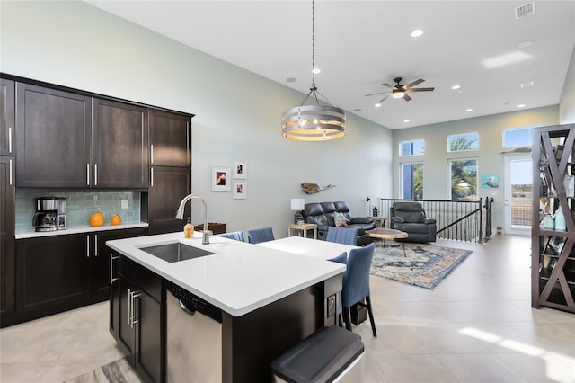 kitchen with sink, hanging light fixtures, a center island with sink, dishwasher, and decorative backsplash