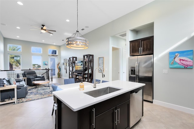 kitchen with sink, a center island with sink, stainless steel appliances, light tile patterned flooring, and decorative light fixtures