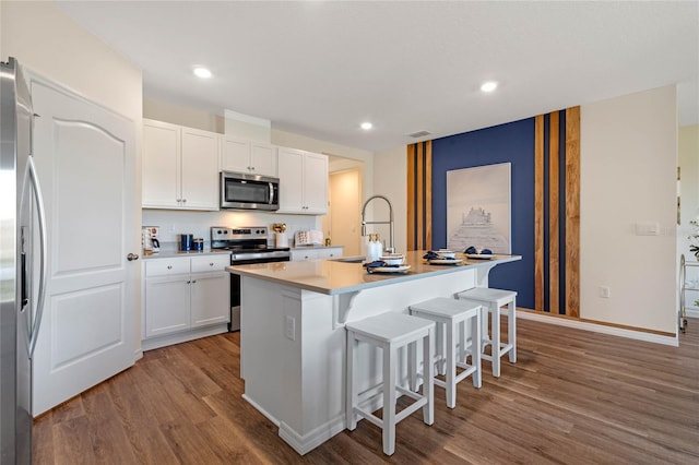 kitchen featuring a breakfast bar, a kitchen island with sink, white cabinetry, stainless steel appliances, and light wood-type flooring