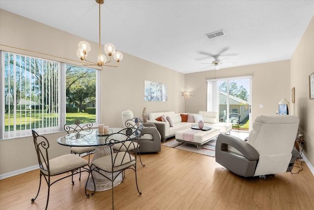 dining space with ceiling fan with notable chandelier and light hardwood / wood-style flooring