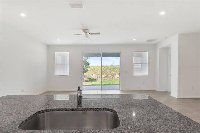 kitchen featuring dark stone countertops, sink, light tile patterned floors, and ceiling fan