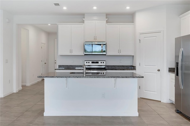 kitchen featuring stainless steel appliances, a kitchen island with sink, dark stone countertops, and white cabinets